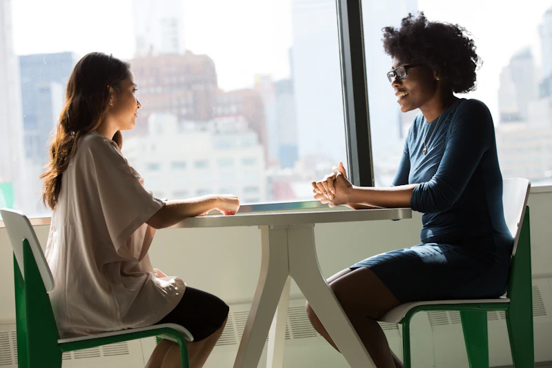 A mentor and a candidate talking at a table by a window
